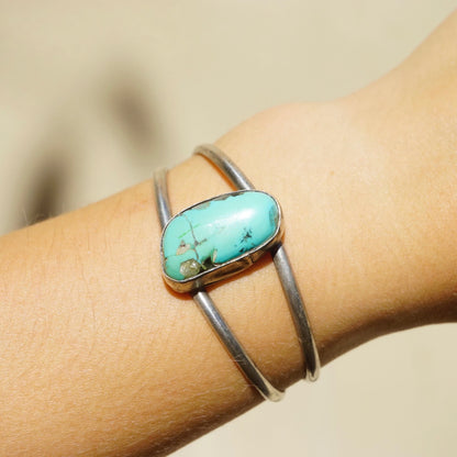 Vintage turquoise stone set in cut out silver cuff bracelet on model's wrist