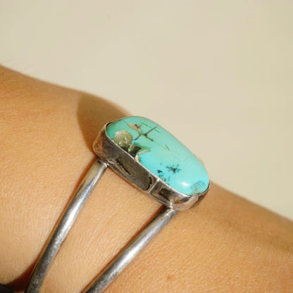 Vintage turquoise and silver cuff bracelet with authentic cut out turquoise stone raised in the center, displayed on a wrist.