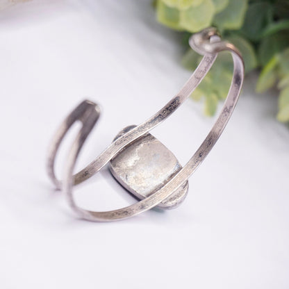 Vintage silver cuff bracelet with raised cutout design and authentic turquoise stone centerpiece, photographed on white background with greenery.