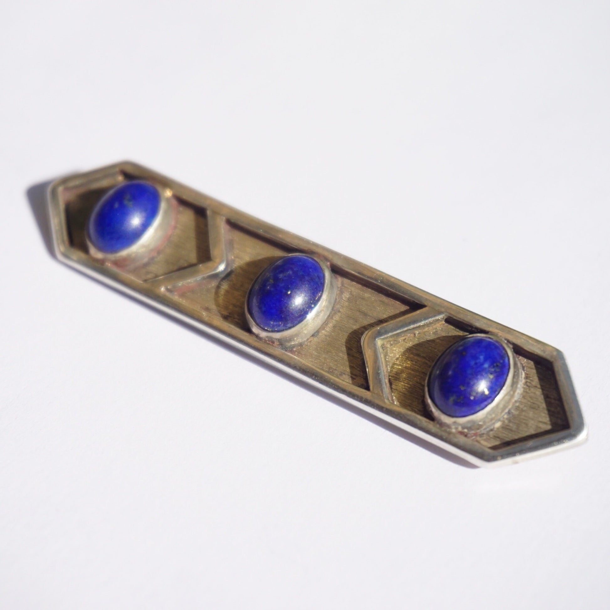 Vintage sterling silver brooch with three round lapis lazuli stones set in an elongated hexagonal shape, displaying a minimalist design and deep blue gemstones against an oxidized silver background.