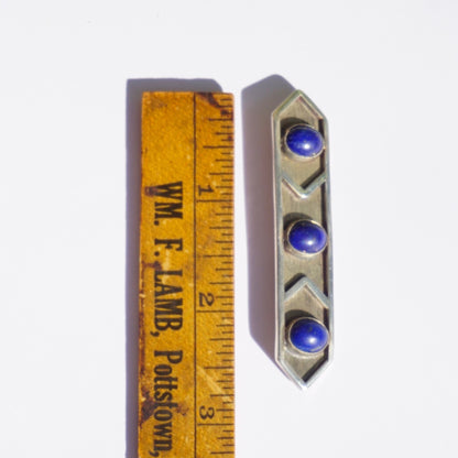 Vintage sterling silver brooch featuring three blue lapis lazuli stones in a minimalist geometric design, measuring against an antique wooden ruler.