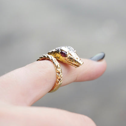 Vintage 14K gold wrap around snake ring featuring ruby eyes and diamond encrusted body on a finger against a gray background.