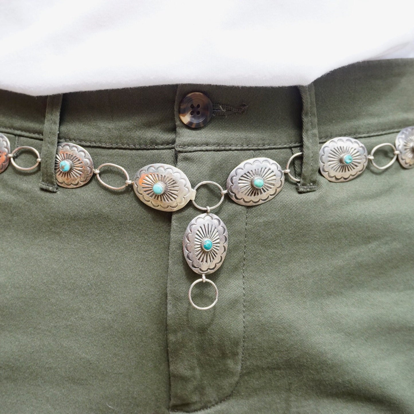 Vintage Native American sterling silver concho belt with turquoise accents, adjustable size, close-up view of silver conchos and connecting rings on olive green fabric, old pawn jewelry piece