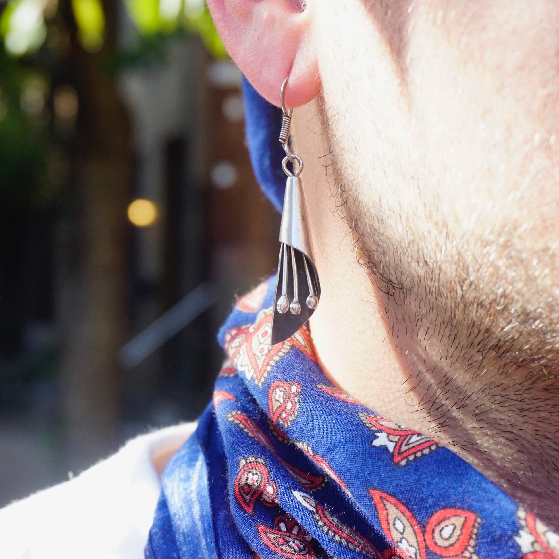 Close-up view of an ear wearing a vintage sterling silver modernist dangle earring with jingle jangles, against a blurred outdoor background.