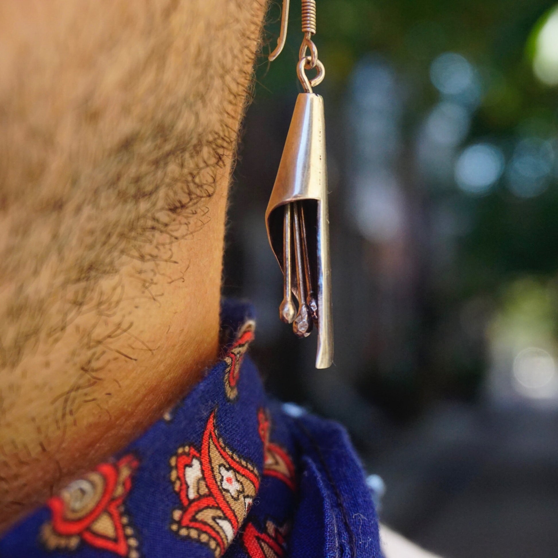 Vintage sterling silver dangle earrings with jingle jangles hanging from a woman's ear, featuring a modernist design. 925 silver chime earrings showcasing intricate patterns on a blue fabric background with a blurred natural setting.