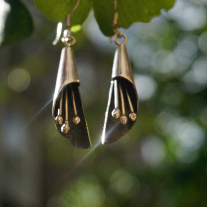 Vintage sterling silver dangle earrings with jingling charms hanging from a modernist petal-shaped design, seen outdoors against a blurred green leaf background.