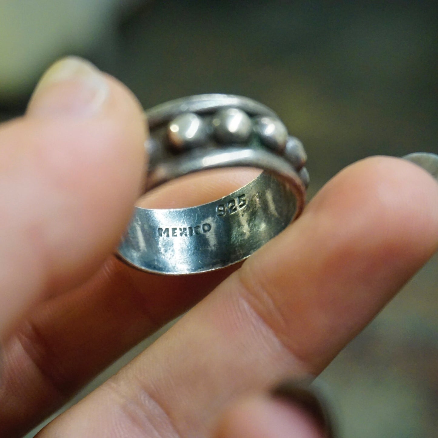 Vintage hammered sterling silver ring with circular silver detail, tarnished finish, and "925 Mexico" stamp, held between fingers, suitable as a men's large silver ring.