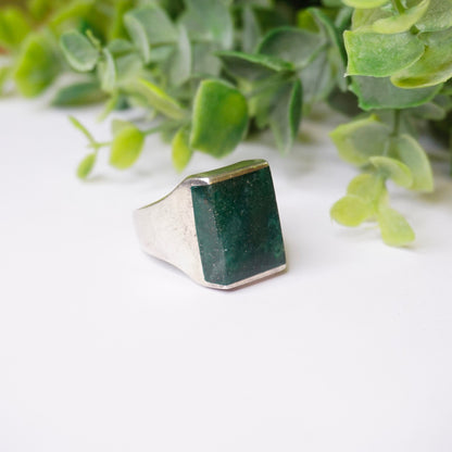 Alt text: Vintage sterling silver ring with a square-shaped green druzy quartz stone, surrounded by green foliage, on a white background.