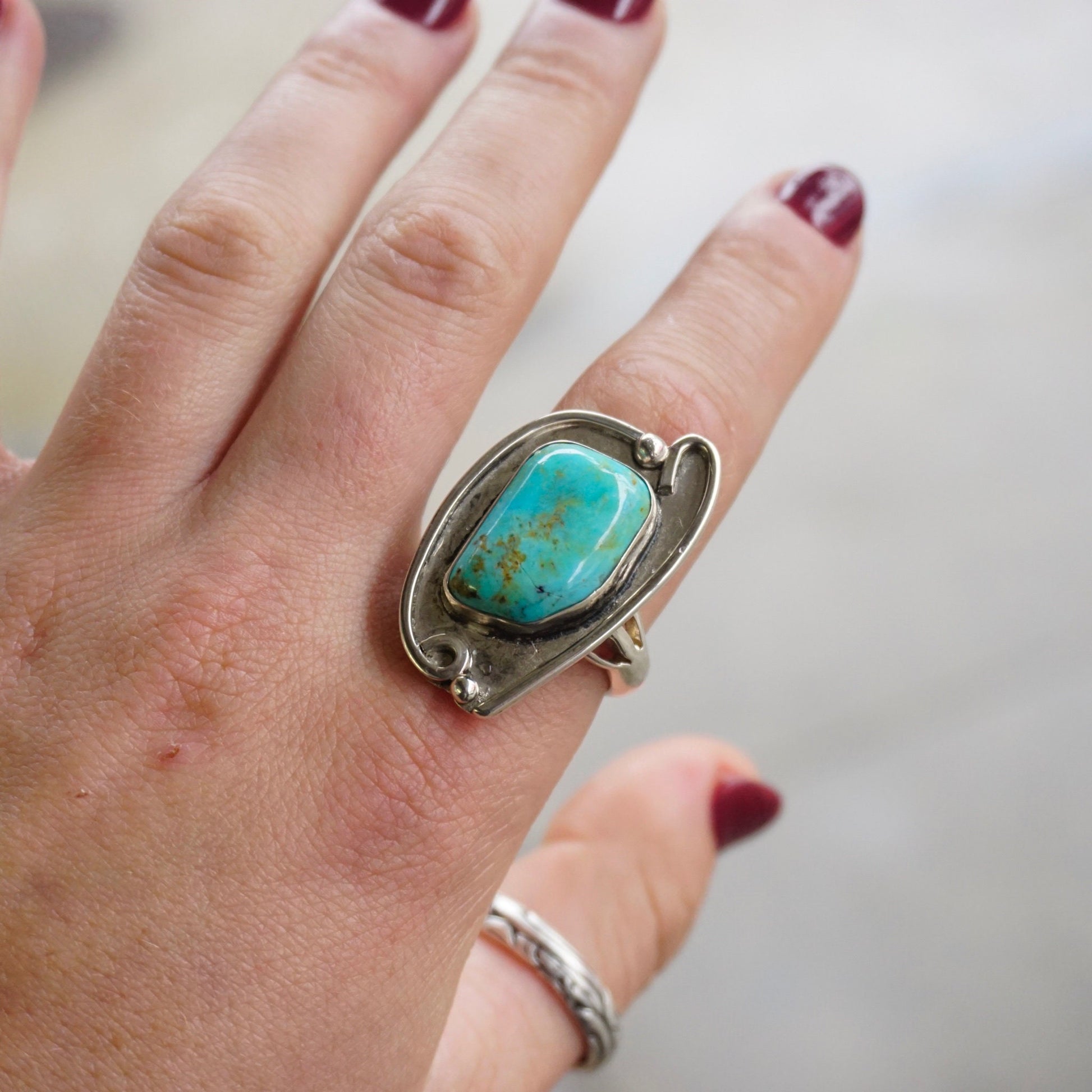 Vintage turquoise sterling silver ring on a hand, featuring a large natural turquoise stone in an ornate silver setting, exemplifying Native American jewelry design.