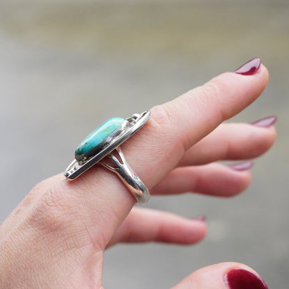 Vintage turquoise sterling silver ring on a finger, showcasing the large natural turquoise stone set in an intricate silver setting, exemplifying traditional Native American jewelry design.