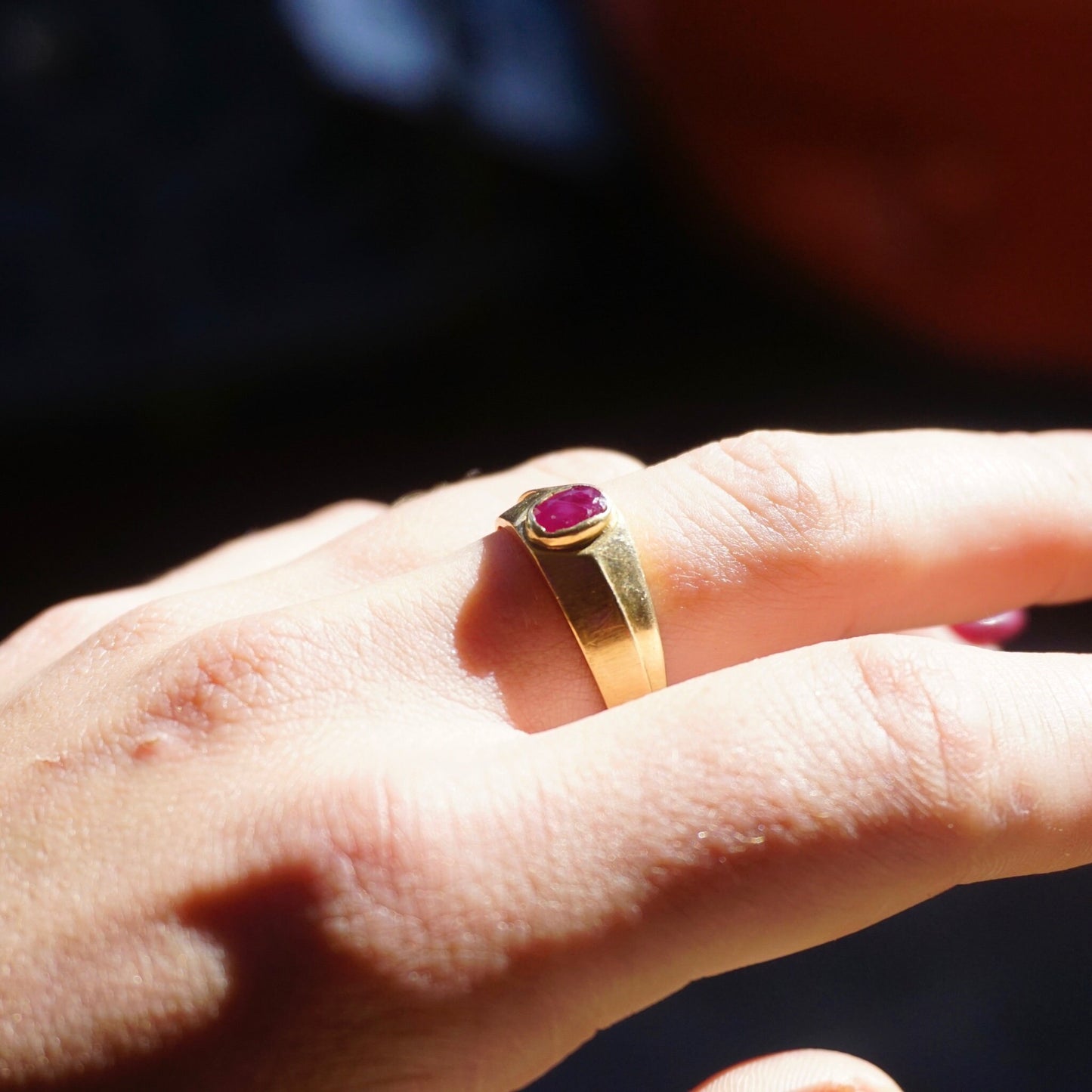 Vintage 10K gold ring with small authentic ruby gemstone on a person's hand, showing the ruby stone and gold band in closeup detail against a dark red background.