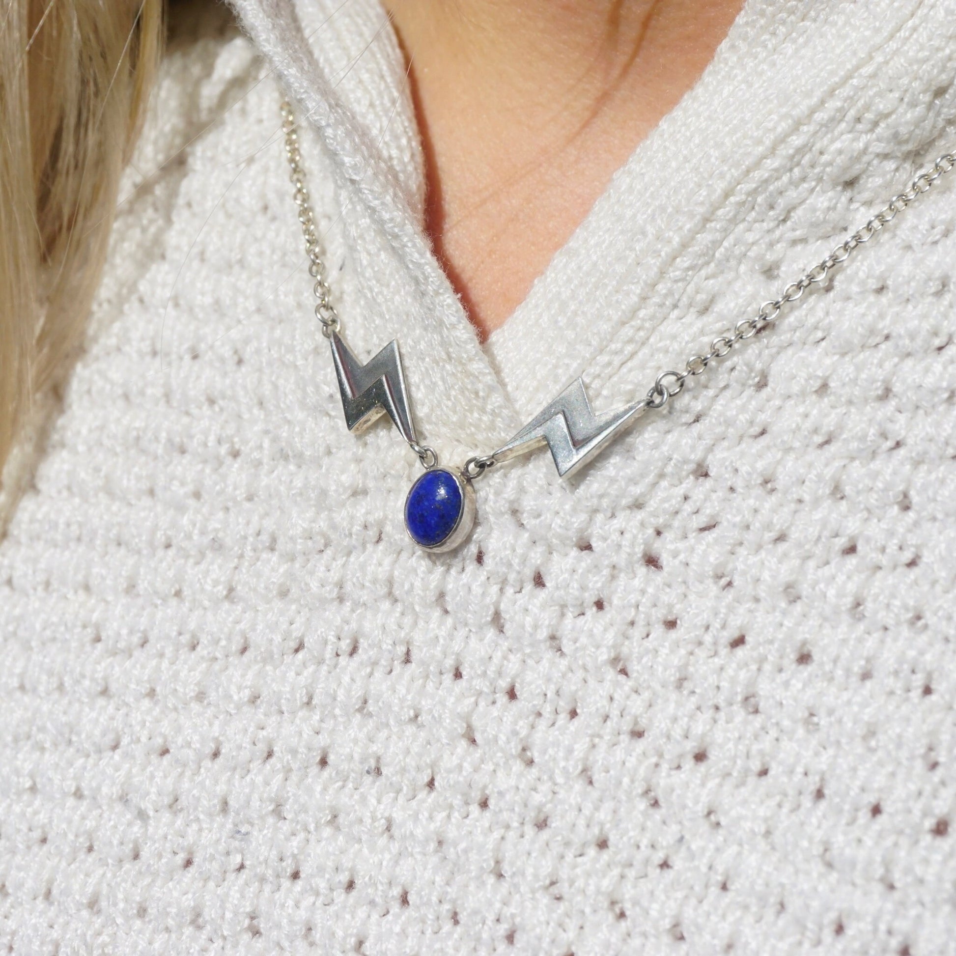 Vintage lapis lazuli silver necklace featuring a unique silver lightning bolt pendant on a silver chain, worn by a person in a white knit sweater.