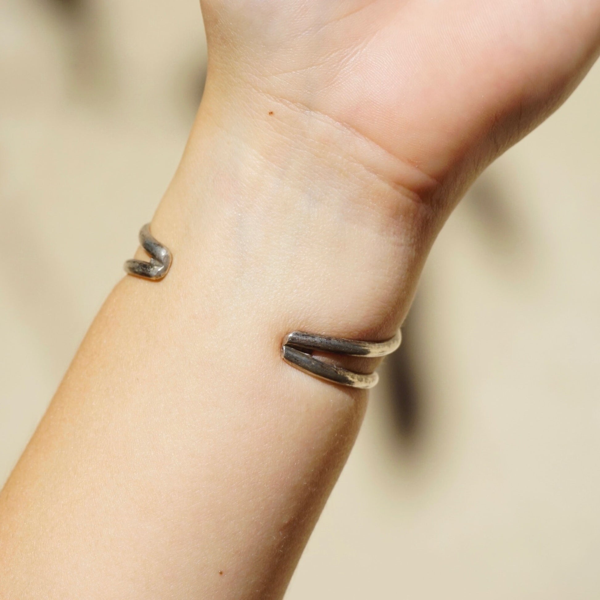 Close up image of a wrist wearing a vintage silver bracelet cuff with a raised turquoise stone accent. The silver cuff bracelet has an open cut-out design that wraps around the wrist, with the genuine turquoise cabochon stone standing out against the tarnished silver metal.