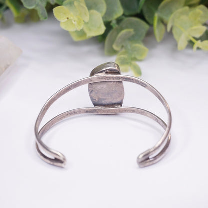 Vintage silver cuff bracelet with raised turquoise stone center, set against a white background with green foliage