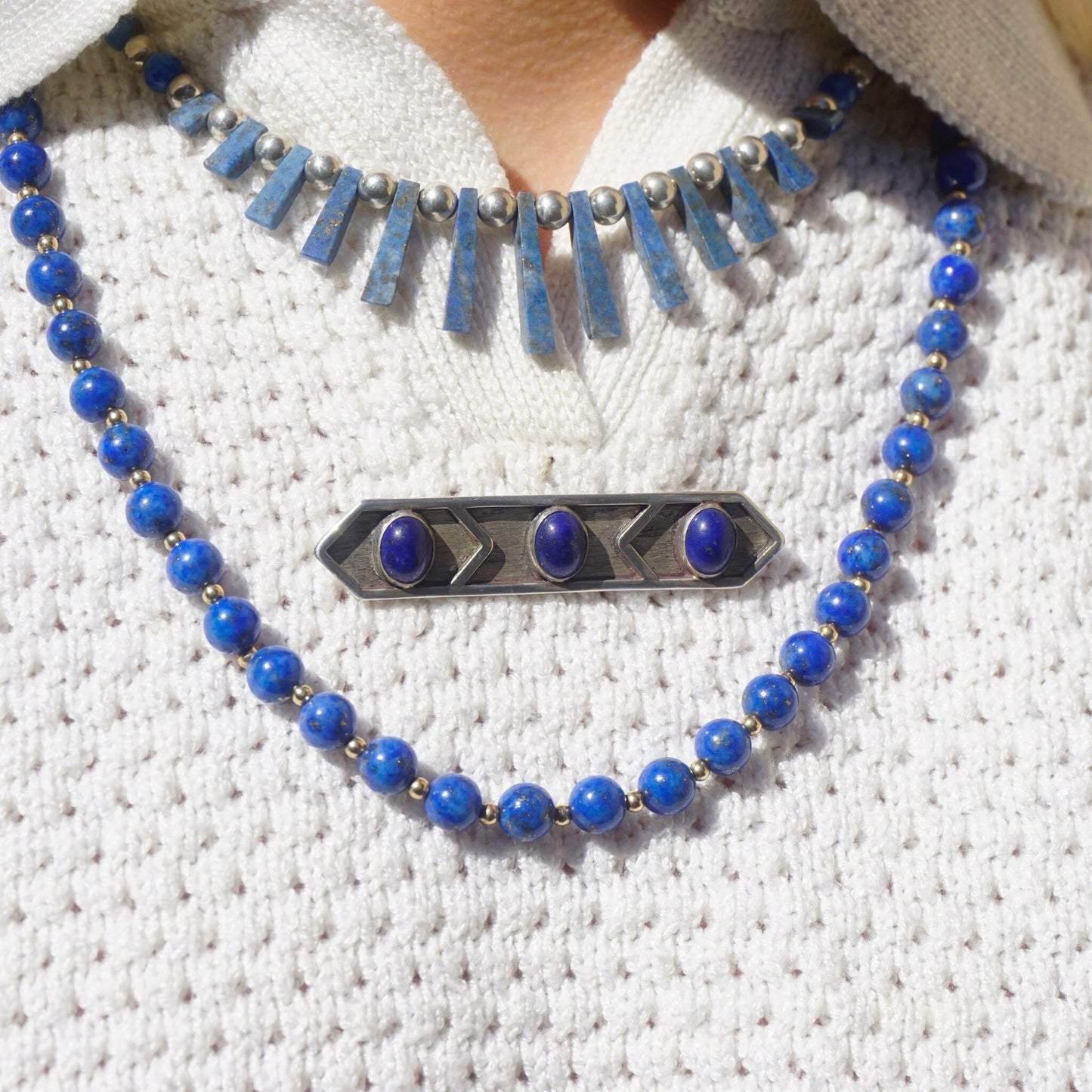 Vintage lapis lazuli and sterling silver brooch necklace featuring a minimalist design with three blue lapis stones set in a geometric silver pendant, displayed on a textured white knit sweater.