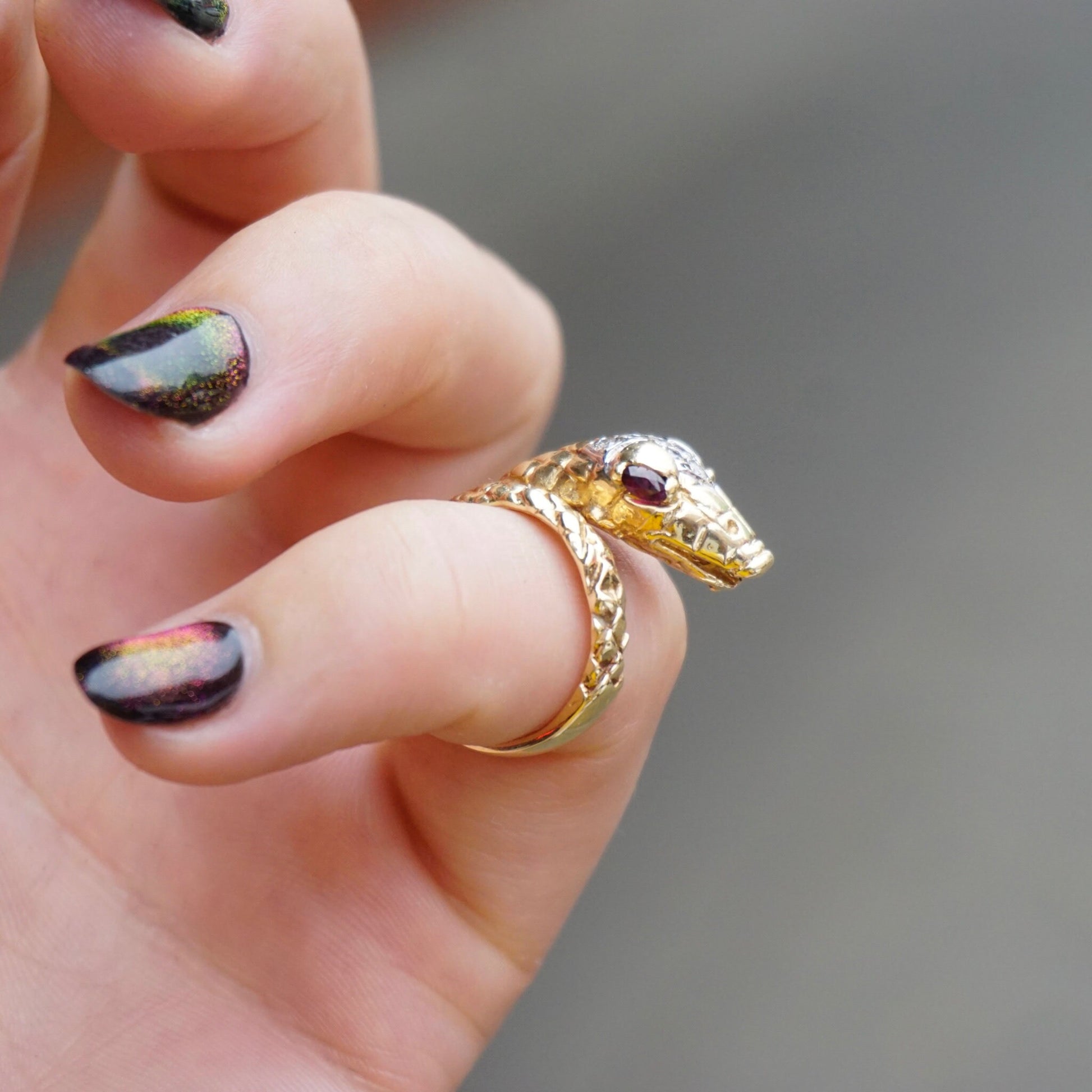 14K gold snake ring with diamond-encrusted body and ruby eyes wrapped around finger