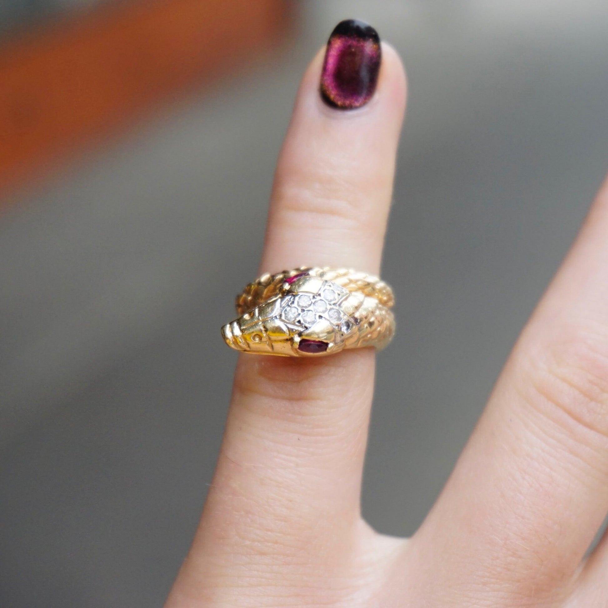 14K gold snake ring with diamond-encrusted body and ruby eyes, worn on finger