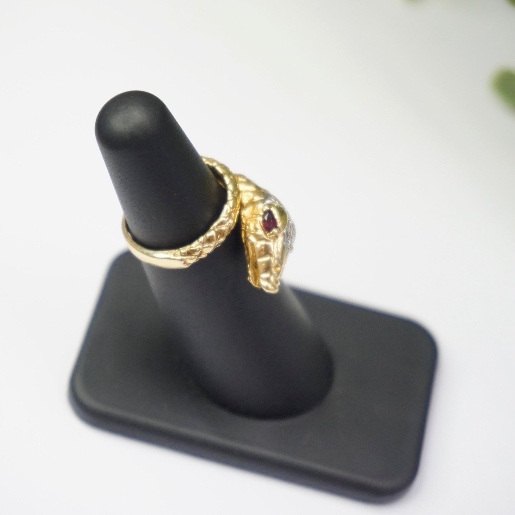 Vintage 14K gold wrap around snake ring featuring ruby eyes and diamond encrusted body on display stand