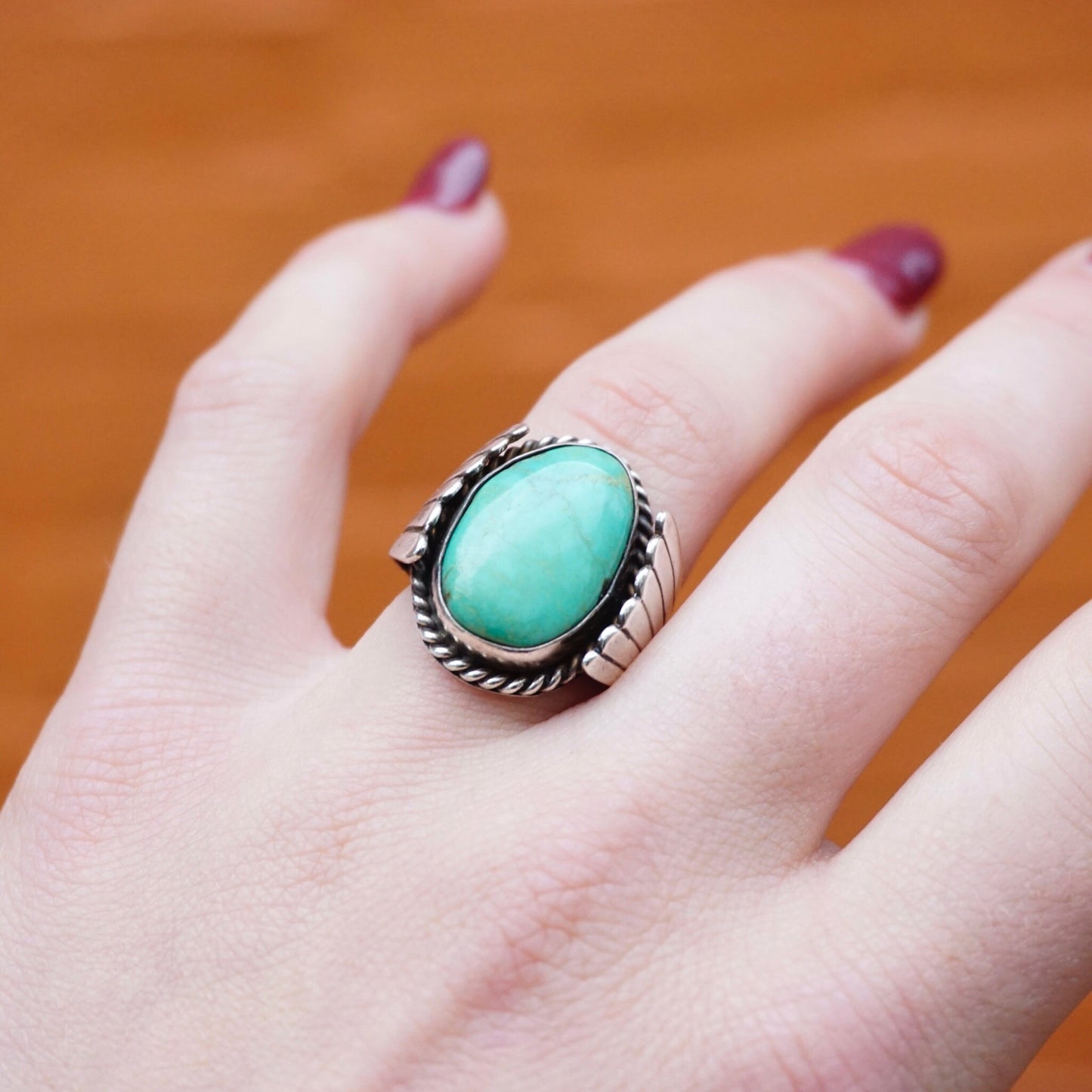 Vintage turquoise sterling silver ring with natural stone on a hand against an orange background