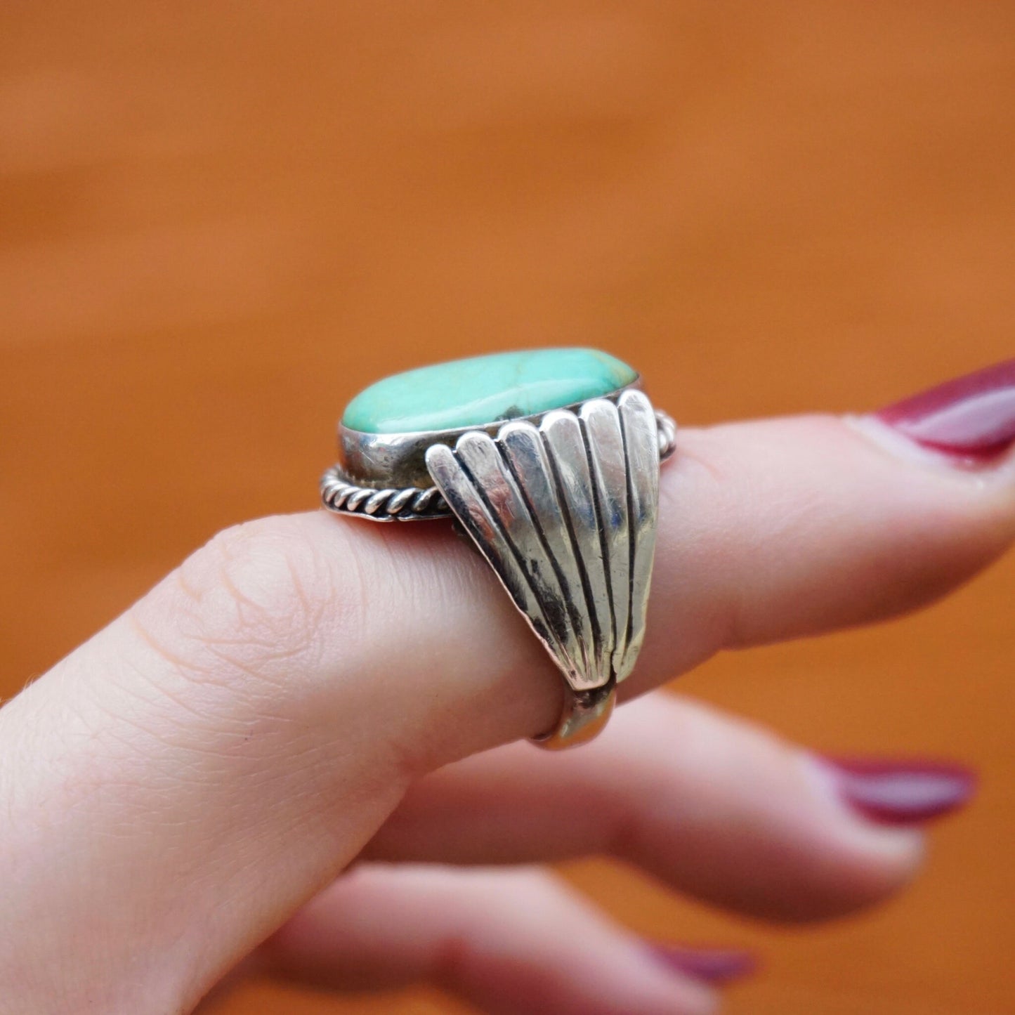 Vintage turquoise sterling silver wing ring on a person's finger against an orange background.