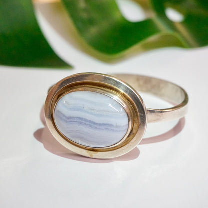 Vintage sterling silver bracelet with oval blue lace agate stone set in raised bezel setting, made by Leenhardt Geneve, against blurred green leaf background