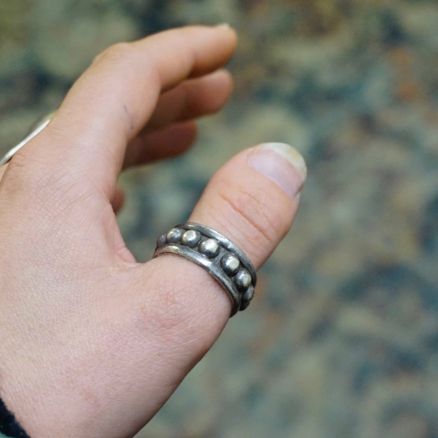 Vintage hammered sterling silver ring with circular dotted details, tarnished patina, made in Mexico 925 silver, shown worn on a person's hand against blurred natural background.