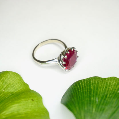 Vintage 10K white gold cocktail ring with deco spiral setting and bright red ruby, elegantly displayed against a white background with green leaf accents.