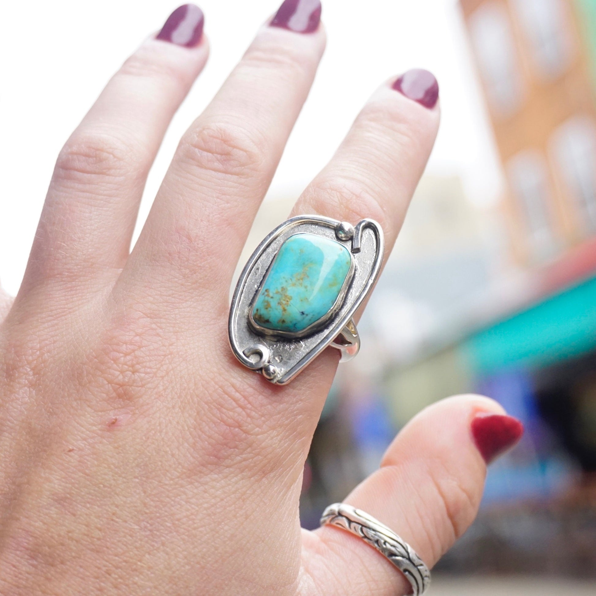 Vintage turquoise sterling silver ring on hand, featuring a large natural turquoise stone in an ornate silver setting, reminiscent of Native American jewelry style.