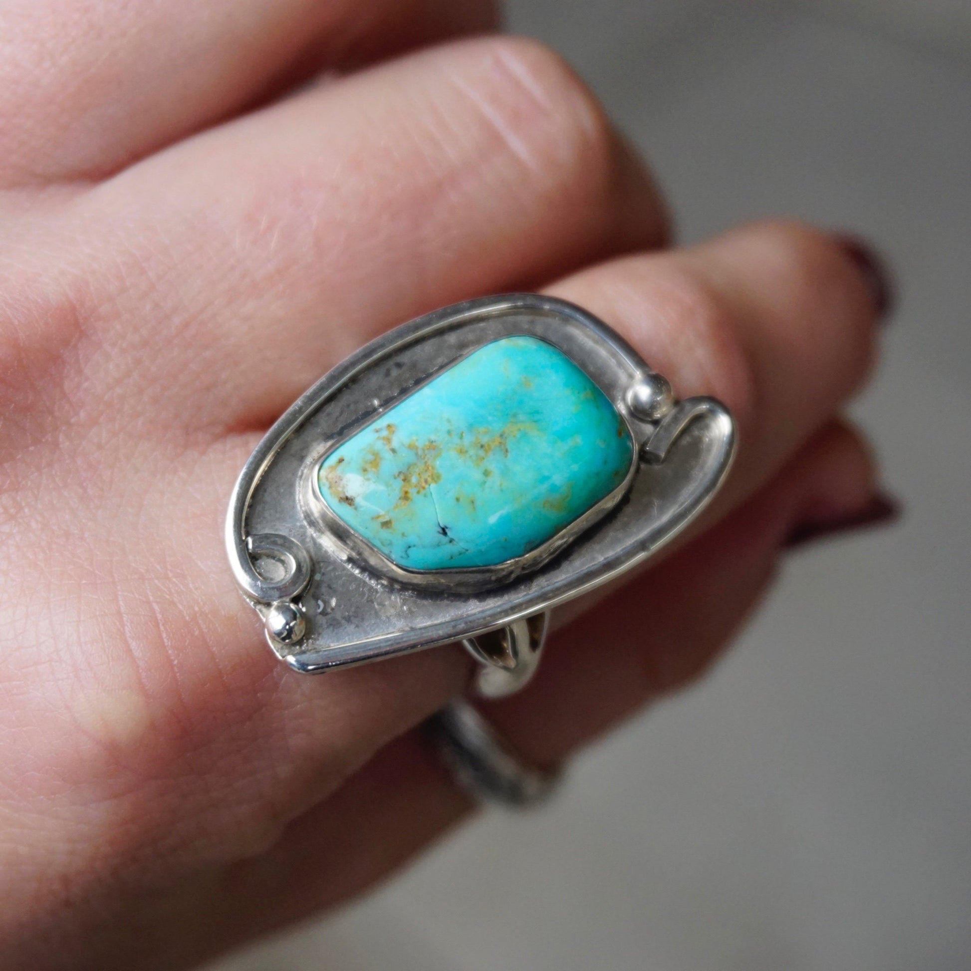 Vintage turquoise sterling silver ring featuring a large natural turquoise stone in an ornate silver setting, held in a hand to showcase the Native American jewelry piece.