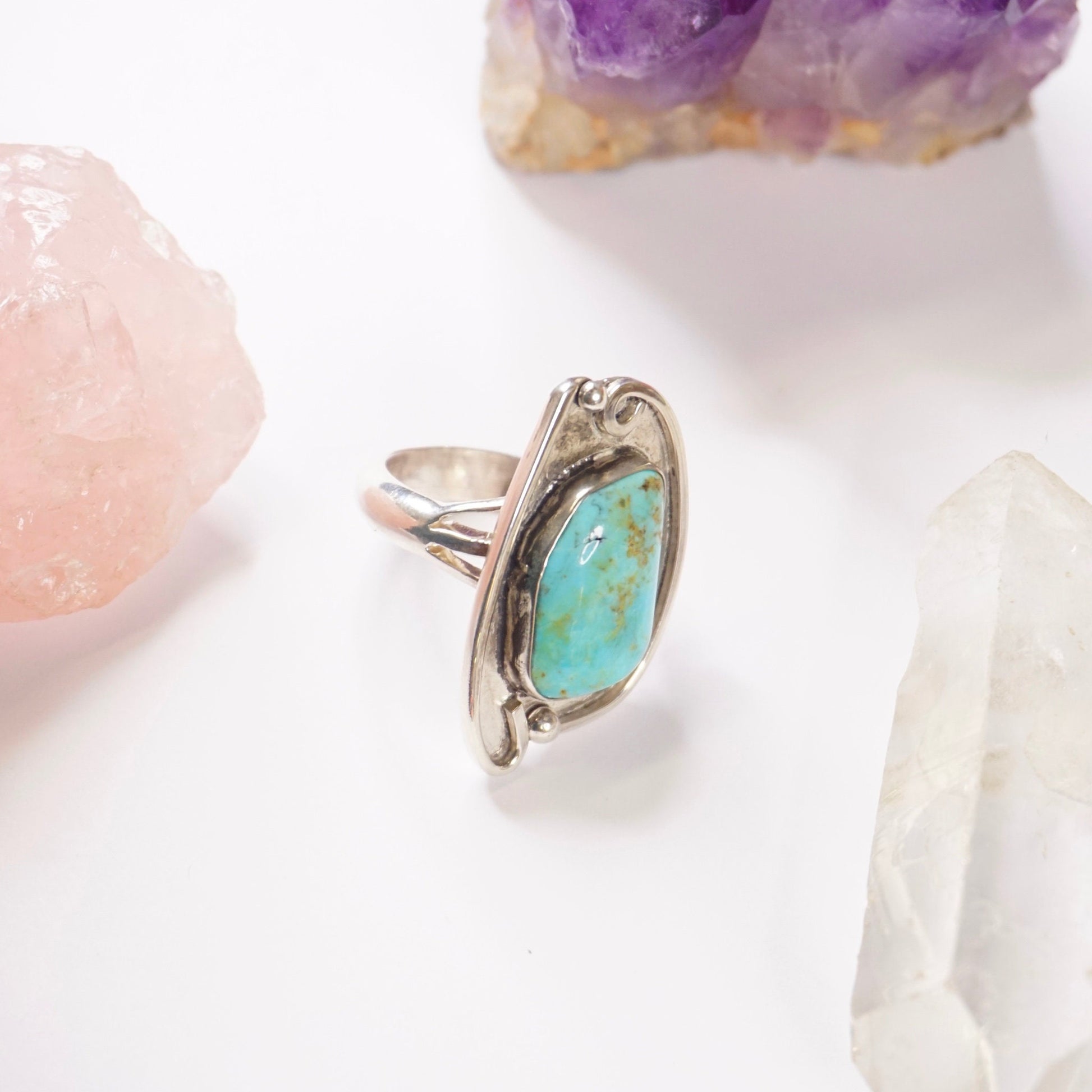 Vintage turquoise sterling silver ring featuring a large natural turquoise stone set in an ornate silver setting, photographed with amethyst and clear quartz crystals, Native American jewelry style silver ring with turquoise centerpiece.