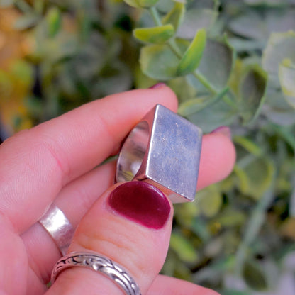 Vintage sterling silver signet ring with thick rectangular face held in hand near green foliage, men's solid 925 silver jewelry ring