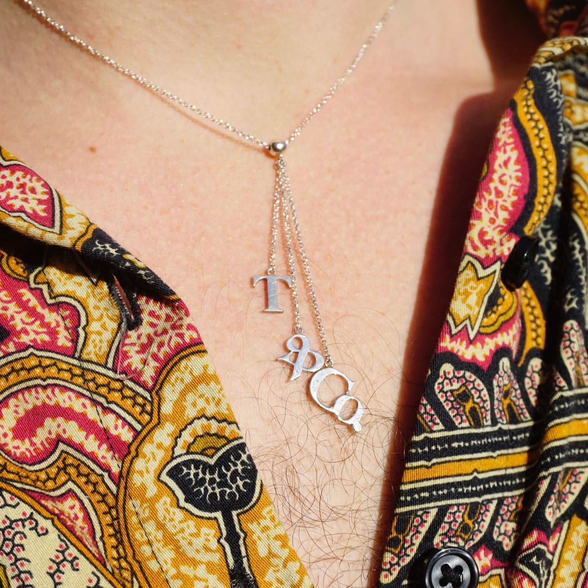 Cropped view of a woman wearing a colorful patterned top and a delicate Tiffany & Co. sterling silver lariat necklace with "T&CO" letters hanging from the chain.