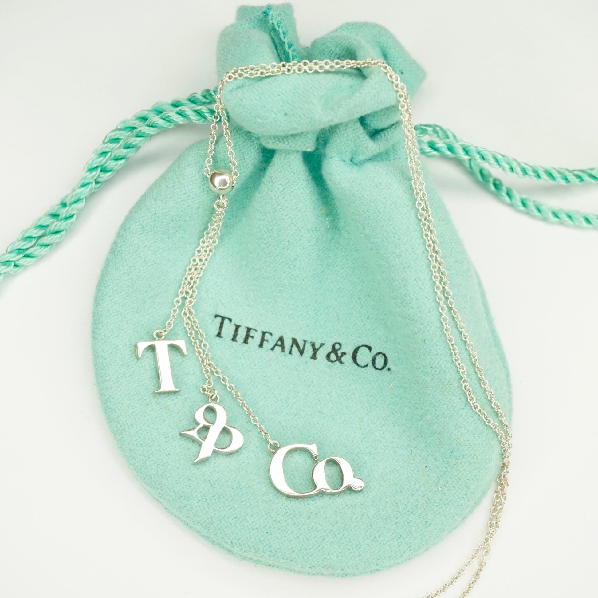 Tiffany & Co. sterling silver lariat necklace with T&CO letters on a teal drawstring pouch.