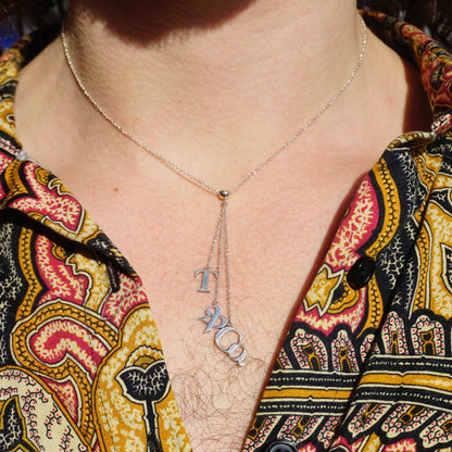 Vintage Tiffany & Co. sterling silver T&CO letter lariat necklace worn on a person's neck against a colorful patterned shirt.