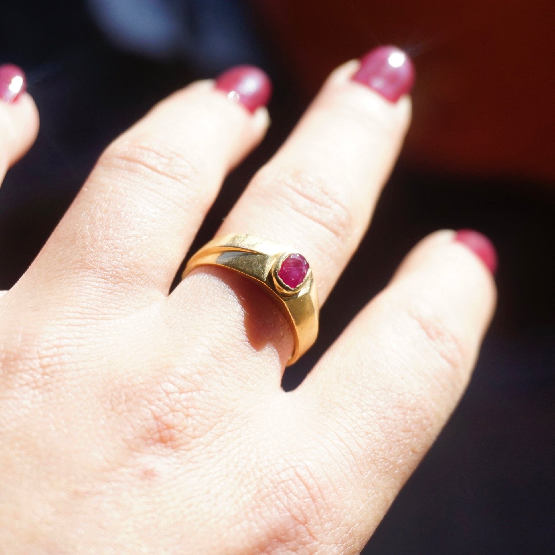 Vintage 10K gold ring with small, round, red ruby gemstone set in the center, shown on a person's finger. The ruby is authentic and the unisex gold band ring is a US size 10 1/4.