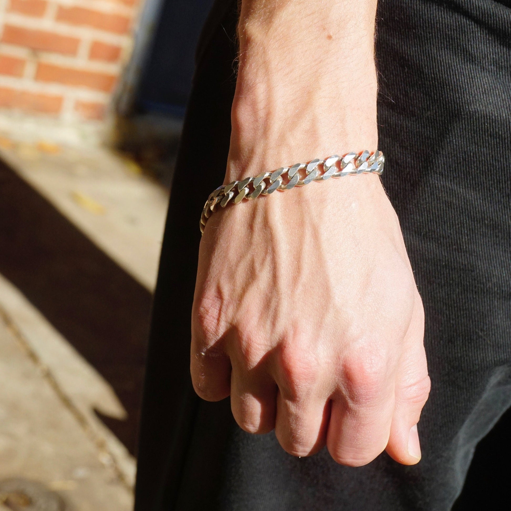 Vintage sterling silver Cuban link bracelet worn on a man's wrist, showing the flat curb link design of the solid silver bracelet made in Italy. The large men's bracelet has a thick chain and polished finish, stamped 925 for sterling silver purity.