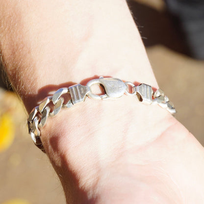 Alt text: Close-up of a vintage sterling silver Cuban link bracelet on a person's wrist, with large flat curb links and a bright polished finish, made in Italy.