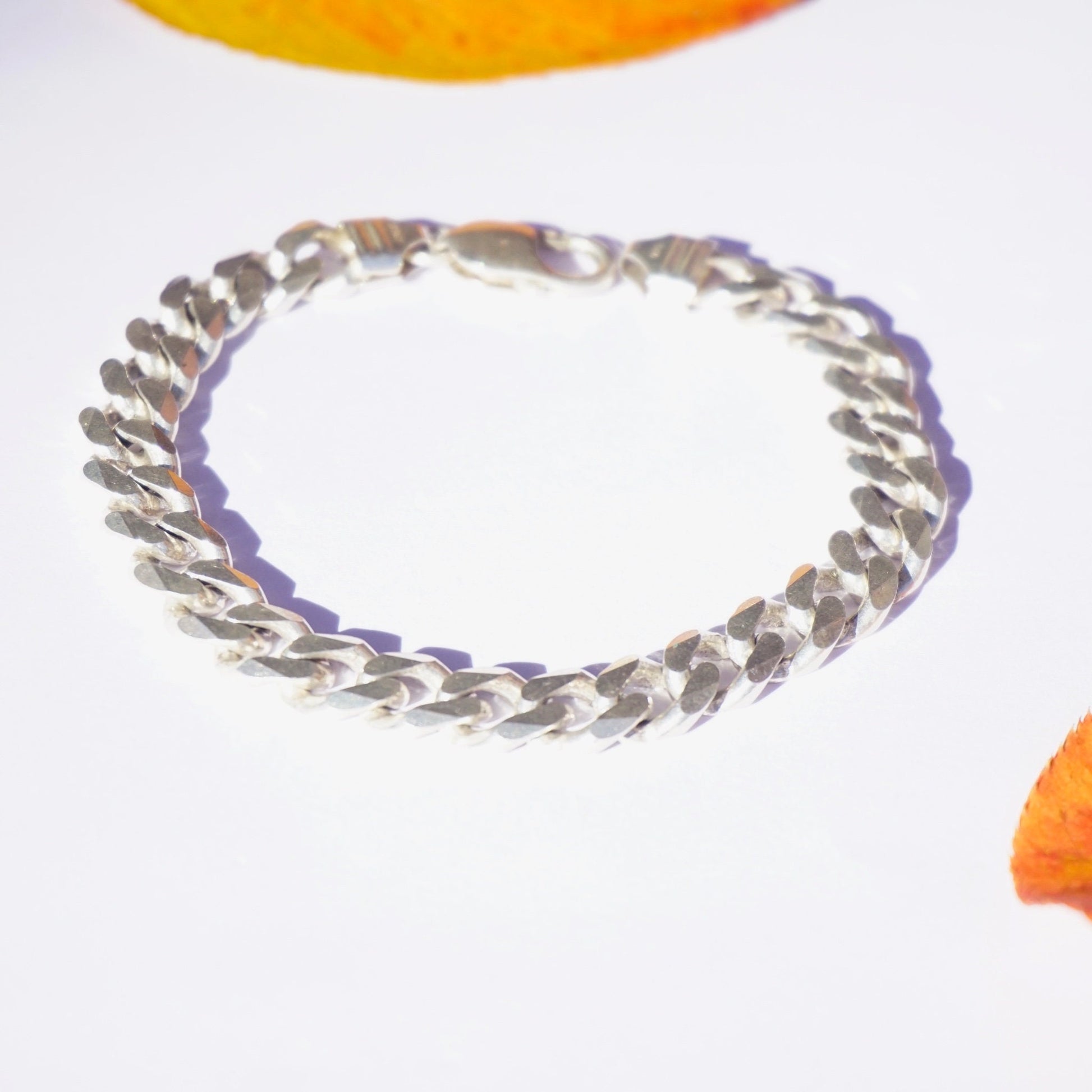 Vintage Sterling Silver Cuban Link Bracelet on white background with orange flower petals