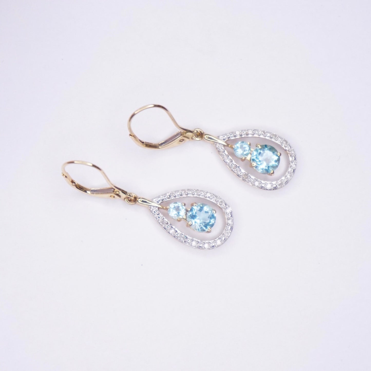 14K gold teardrop earrings with aquamarine and accent diamonds, gold drop earrings with light blue gemstone center stones surrounded by a halo of small diamonds, hung from gold lever back earring hooks