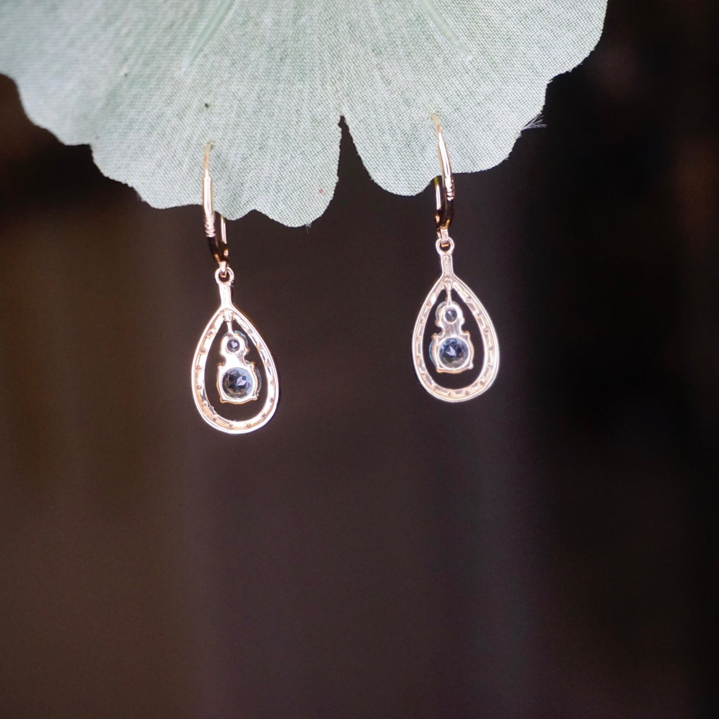 14K gold teardrop earrings with aquamarine and diamond accents, hanging from green leaf