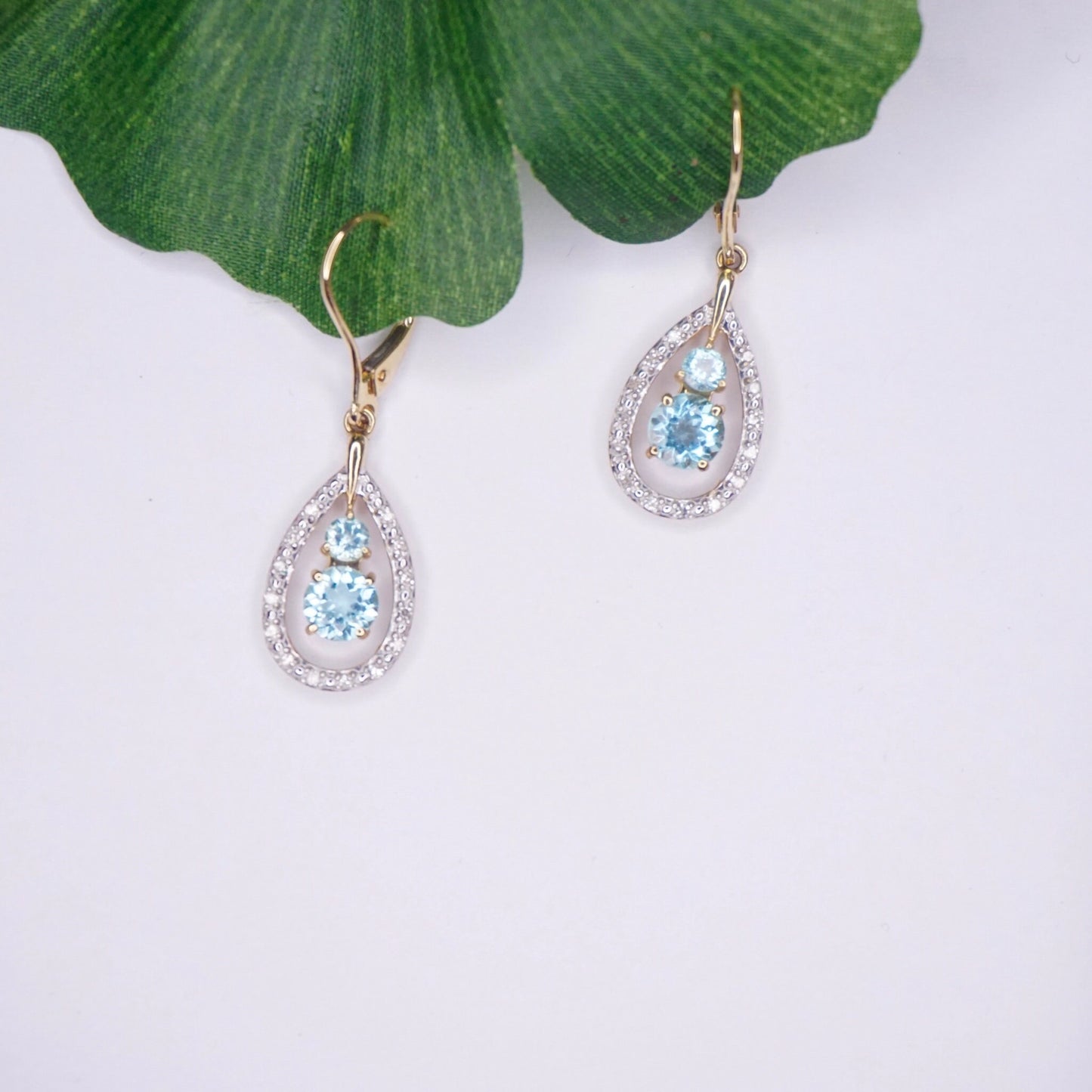 Vintage 14K gold teardrop earrings featuring aquamarine gemstones and accent diamonds, hanging from green leaf with white background.