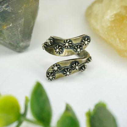 Vintage sterling silver beaded flower twist wrap around ring, made in Taxco, Mexico, 925 silver ring with delicate floral details, shown with green leaves and gemstones in the background.