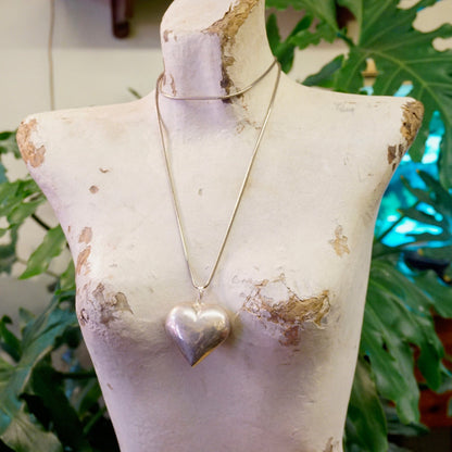 Vintage silver heart pendant necklace on old white mannequin bust surrounded by green foliage