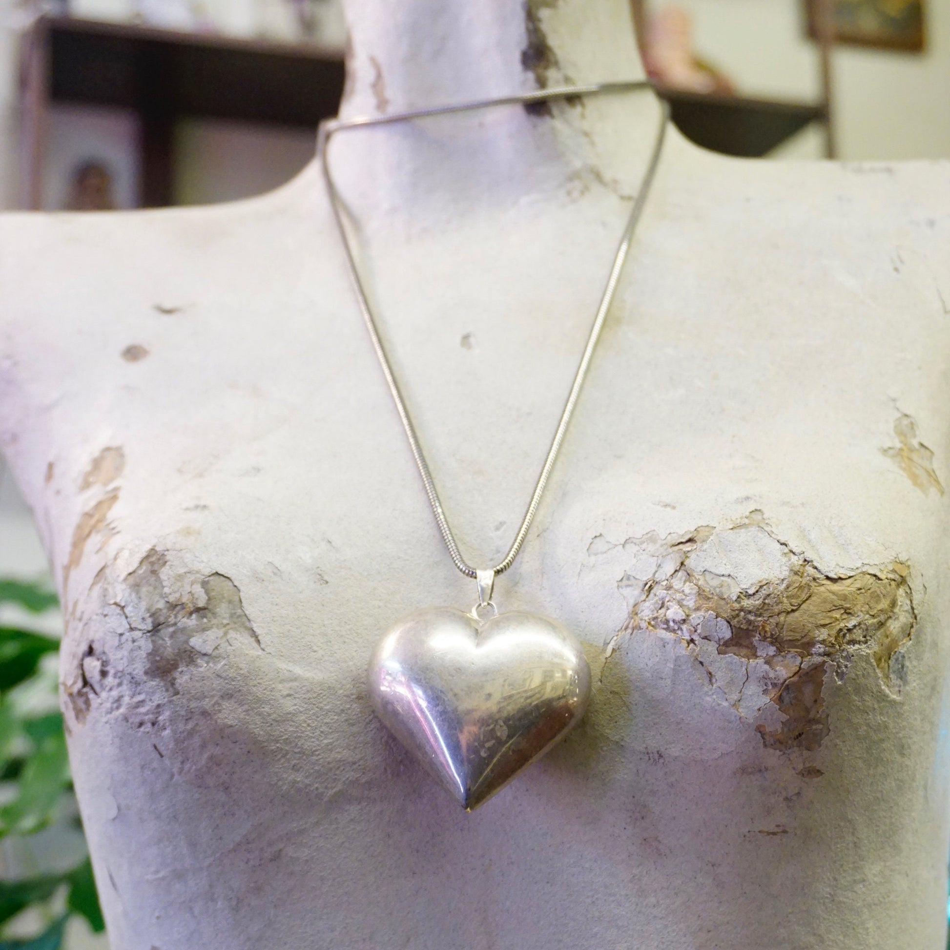 Vintage silver heart pendant necklace on silver rope chain against weathered white background