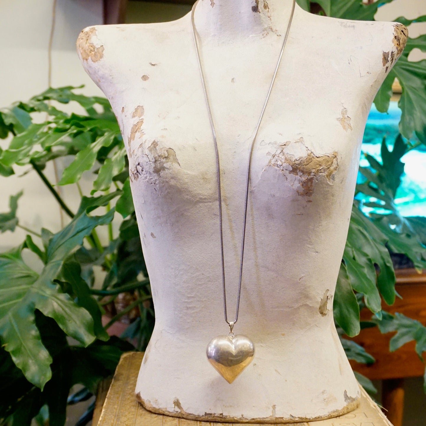 Vintage silver heart pendant necklace on distressed mannequin surrounded by greenery