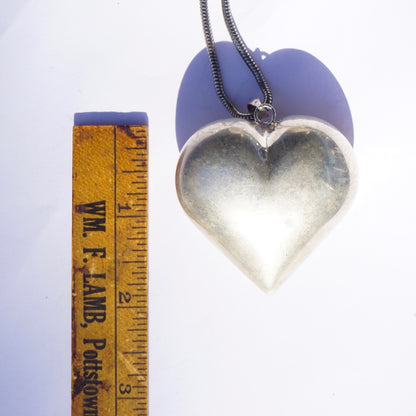 Vintage silver heart pendant necklace on purple heart-shaped background next to wooden ruler, large puffed heart charm on oxidized silver chain, statement 925 jewelry piece