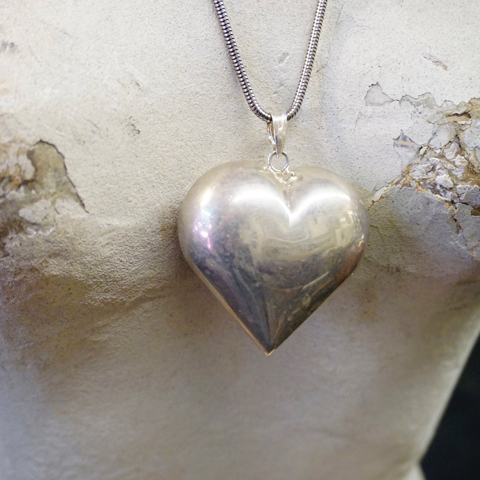 Vintage silver puffy heart pendant necklace on silver rope chain against textured background