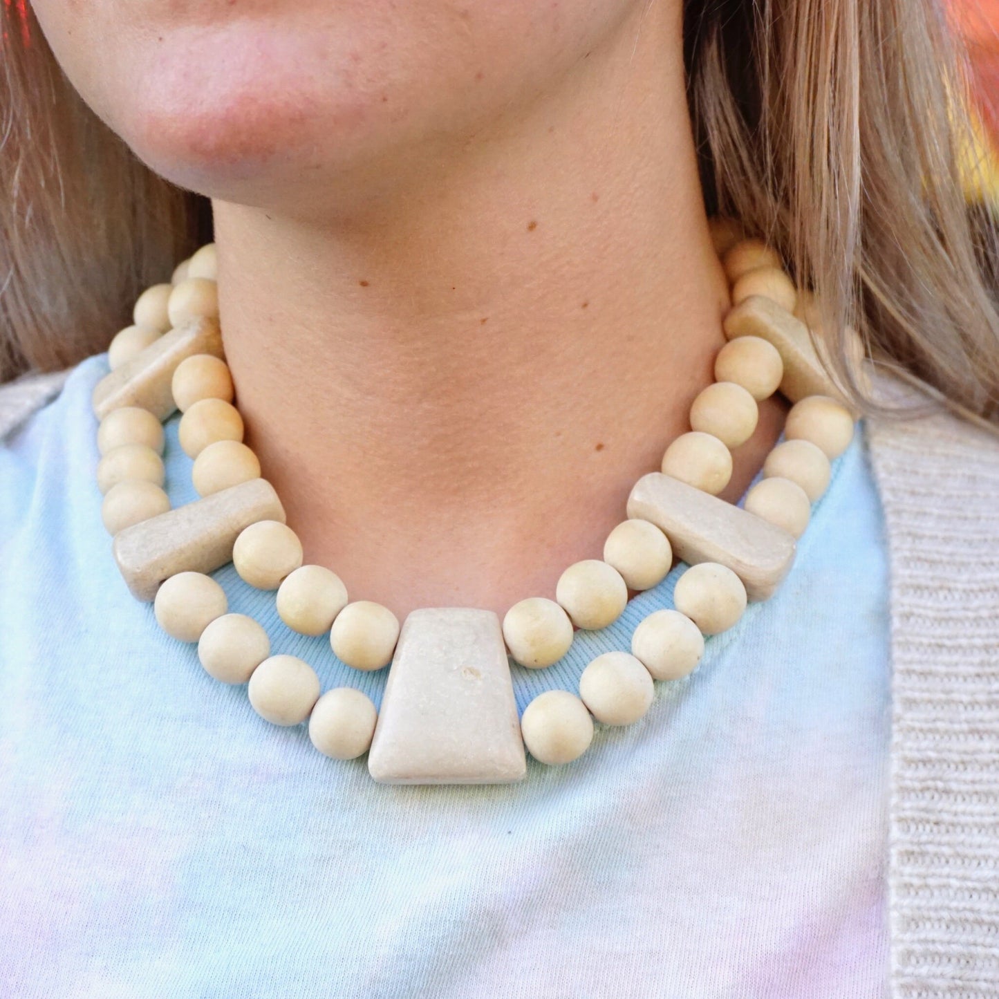 Vintage Gerda Lynggaard Monies chunky wooden two-strand collar necklace with beige wooden beads and single white stone bead worn around a woman's neck against a pastel shirt.