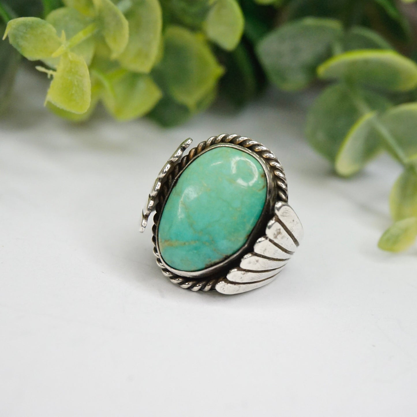 Vintage turquoise sterling silver ring featuring a natural turquoise stone set in an ornate silver band with wing or leaf details, handcrafted Native American 925 silver jewelry displayed with succulent greenery in the background.