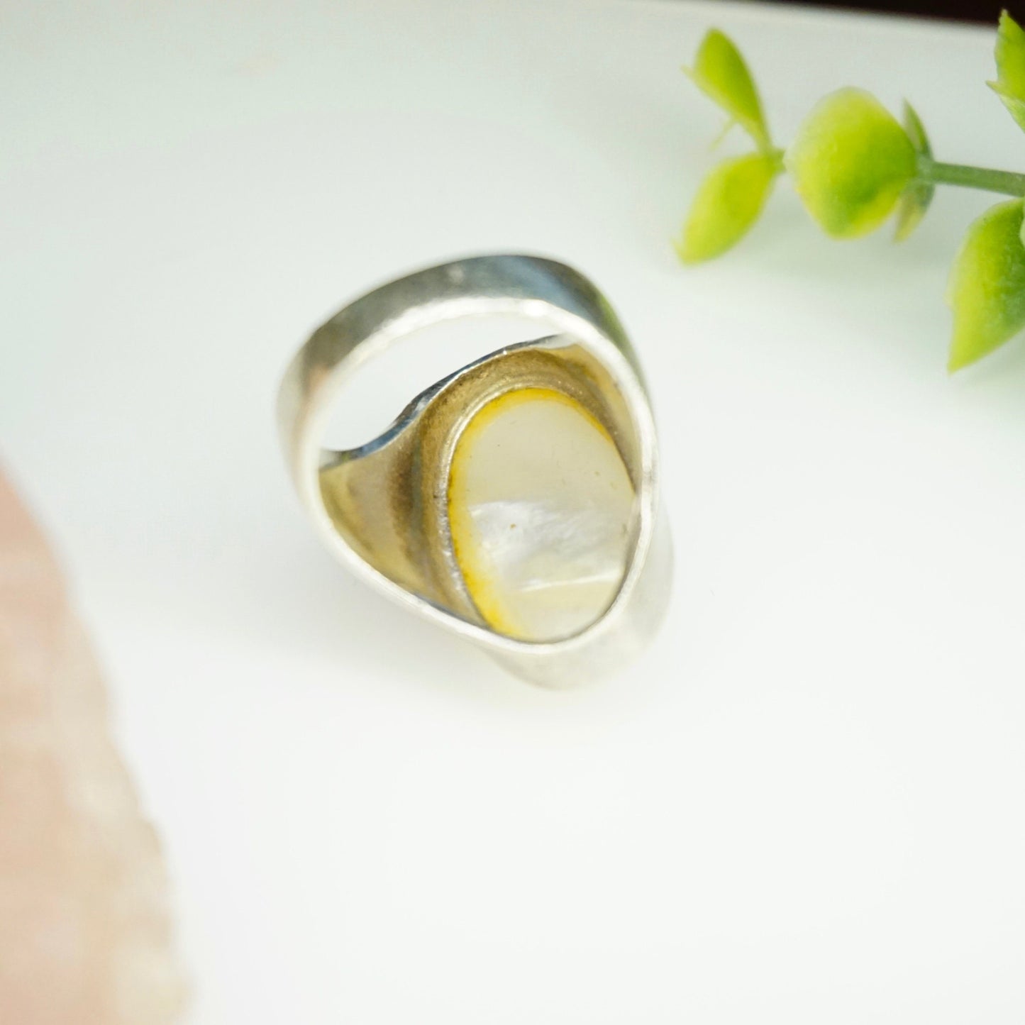 Vintage sterling silver ring with iridescent mother of pearl inlay on a light background with green foliage accents